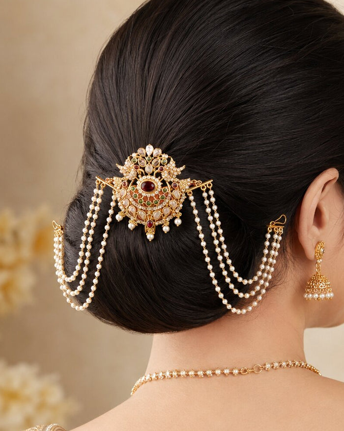 A woman shown from the back wearing a gold and pearl traditional Indian hair accessory (hair pin) with dangling chains, matching gold earrings, and a pearl necklace.