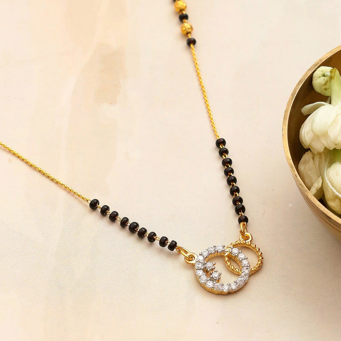 Gold necklace with black beads and a circular pendant on a beige background